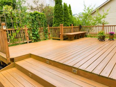 This picture is of a large wooden deck with a bench next to a garden.